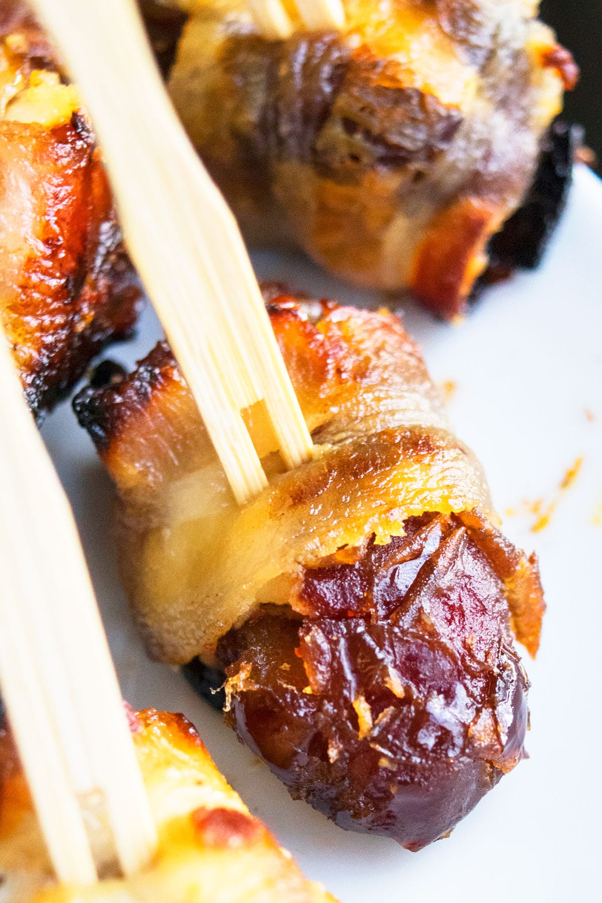 Easy Bacon Wrapped Dates With Toothpick on White Dish.