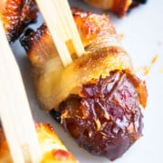 Easy Bacon Wrapped Dates Stuffed With Goat Cheese And Secured With Toothpick on White Dish.