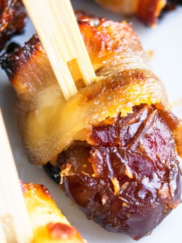 Easy Bacon Wrapped Dates Stuffed With Goat Cheese And Secured With Toothpick on White Dish.