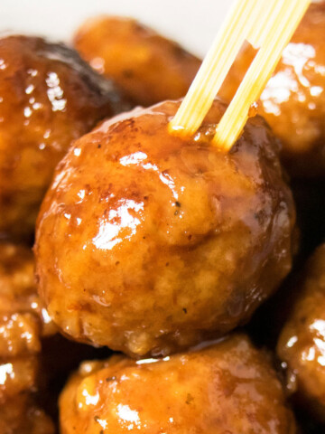 Bamboo toothpick being pushed into the best easy instant pot grape jelly meatballs.