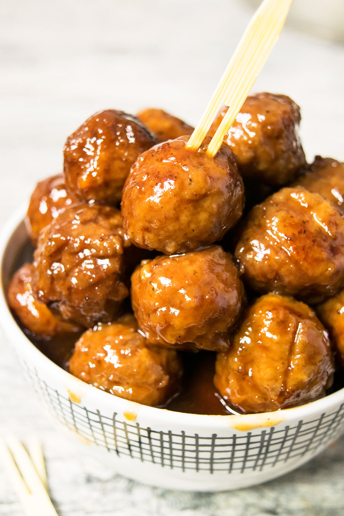 White bowl filled with cocktail meatballs with sauce dripping on the sides. 