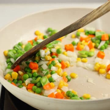 Veggies and onions being sauted in oil in a nonstick pan.