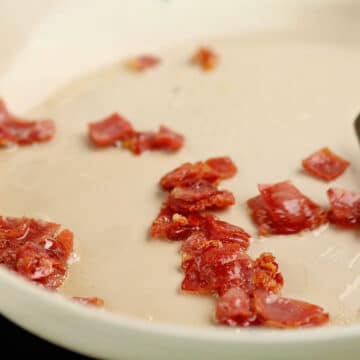 Bacon being fried in white nonstick pan.