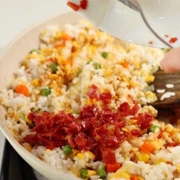 Crispy cooked bacon being added to other ingredients in nonstick pan.
