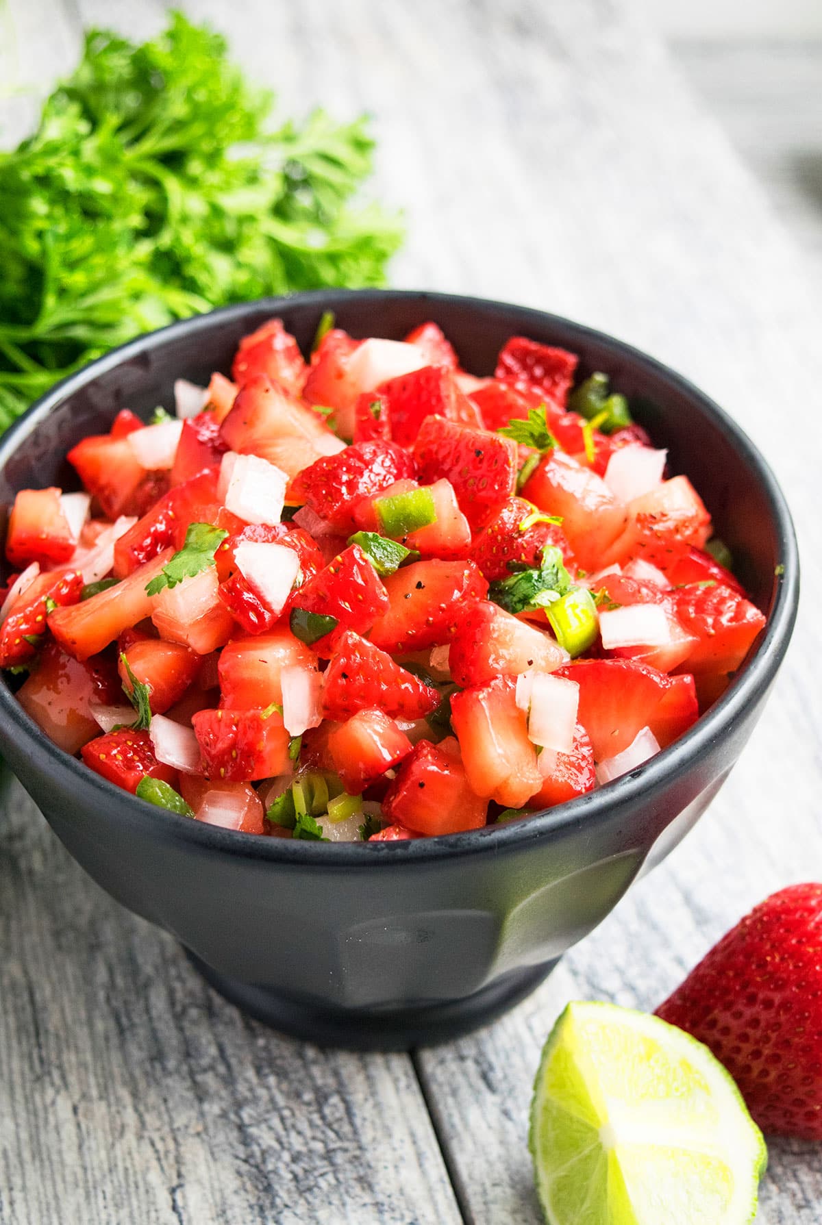 Fresh berry salsa in black bowl on rustic gray background. 
