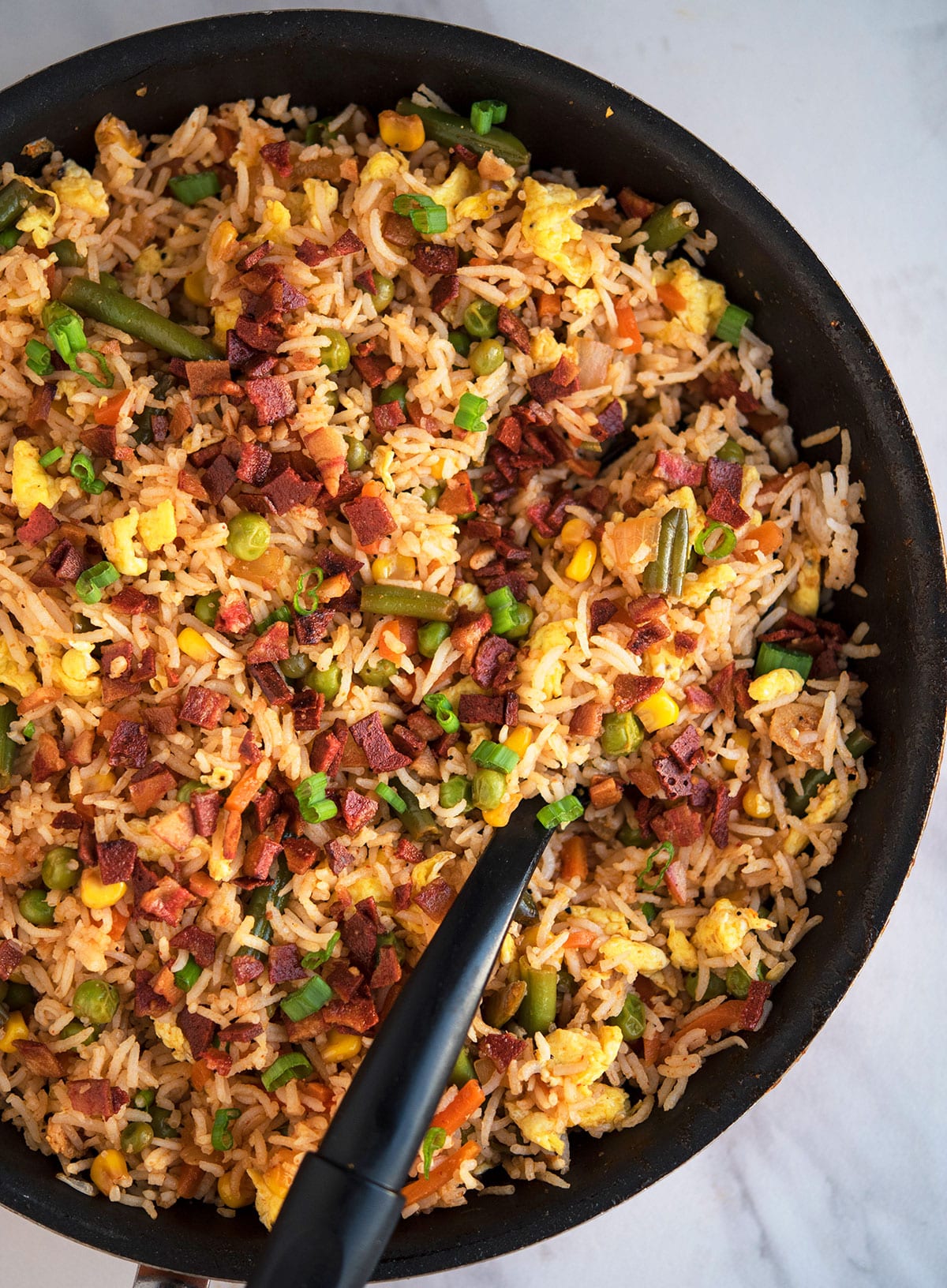 Easy one pot bacon fried rice with black spoon on white marble background.