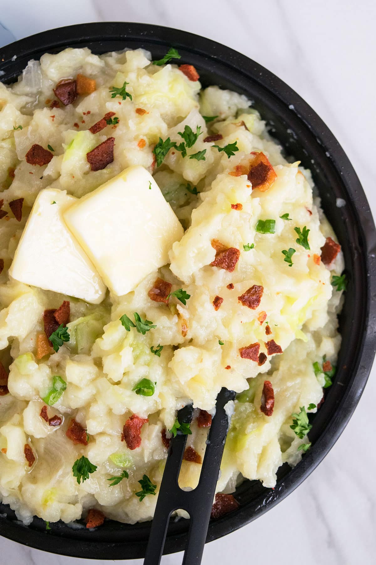 Easy one pot colcannon with butter and crumbled bacon topping on white marble background.