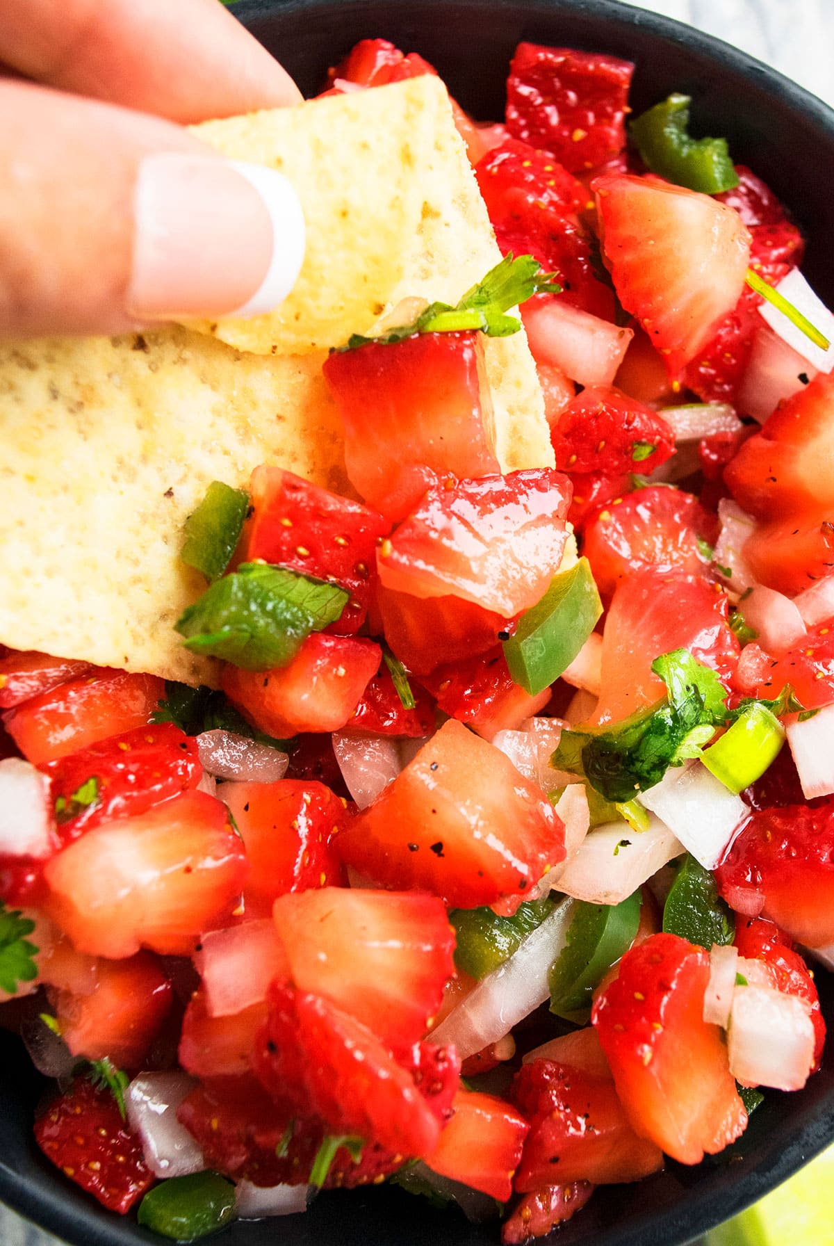 Tortilla scooping Mexican dip from black bowl.  