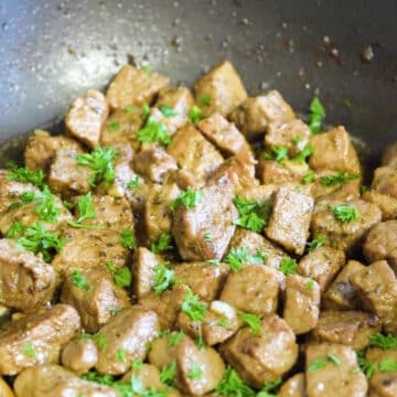 Fresh parsley garnish added on top of cooked beef cubes.