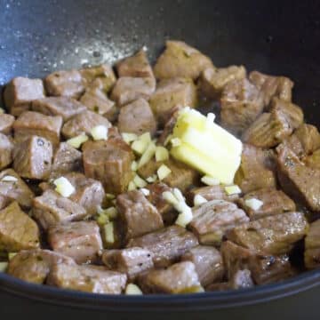 Garlic and butter added to golden brown beef cubes.