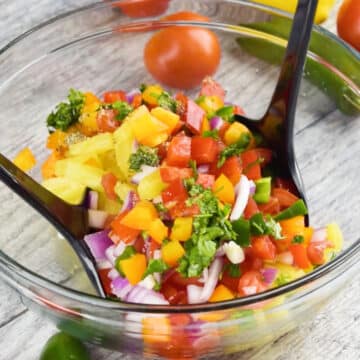 Ingredients being mixed together in glass bowl with two salad spoons.