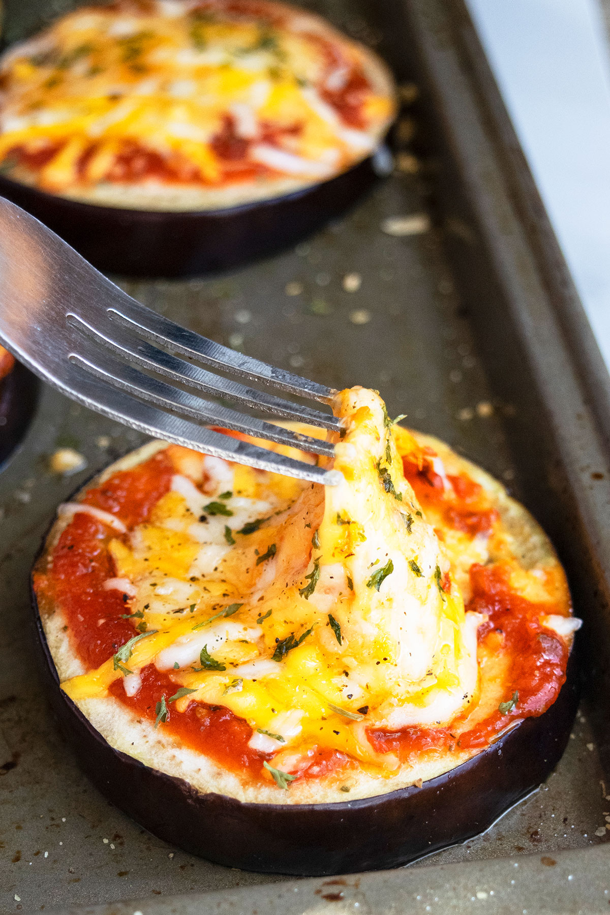 Fork showing a cheese pull on eggplant pizza on baking tray.