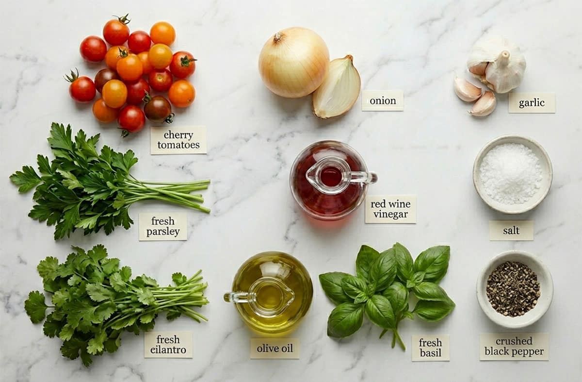 Ingredients for recipe on white marble background- fresh herbs, salt, pepper, onion, garlic, olive oil, cherry tomatoes, red wine vinegar. 