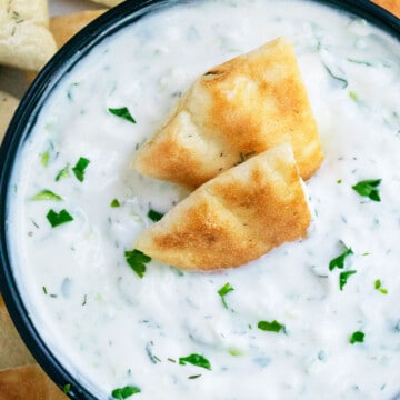 Best creamy easy homemade Greek Tzatziki Sauce in black bowl with pita bread slices.