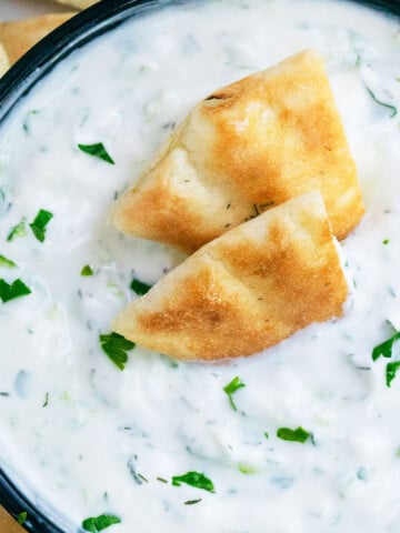 Best creamy easy homemade Greek Tzatziki Sauce in black bowl with pita bread slices.