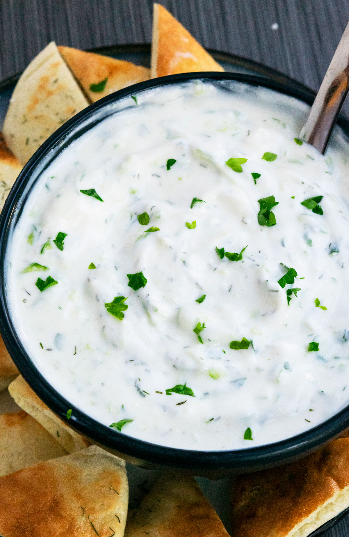 Cucumber Sauce or Dip in black bowl on a tray with sliced pita breads.