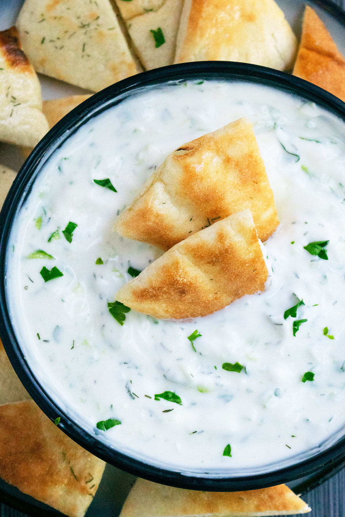 Easy homemade Tzatziki Sauce in black bowl with pita bread slices.