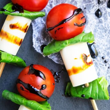 Easy homemade mini caprese skewers or kabobs appetizer with balsamic glaze on charcoal gray dish.