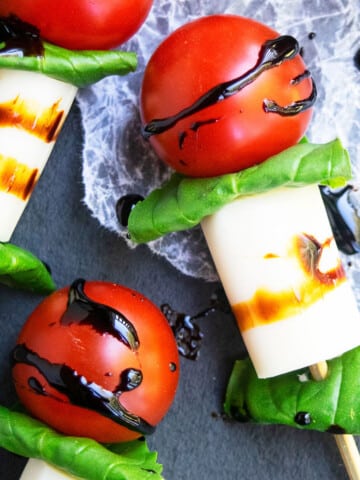 Easy homemade mini caprese skewers or kabobs appetizer with balsamic glaze on charcoal gray dish.