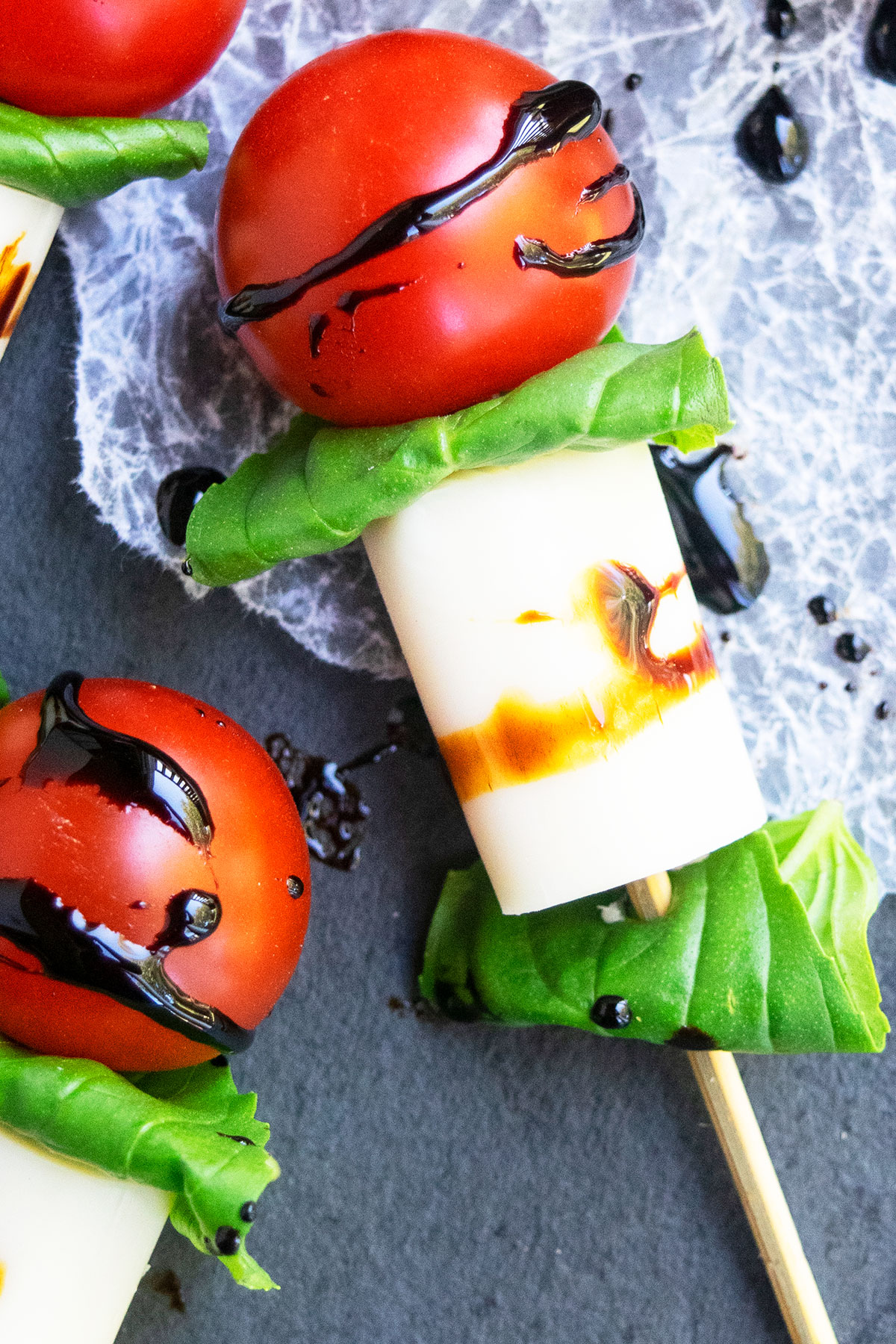Closeup shot of appetizer on stick on charcoal gray dish with crumpled wax paper.