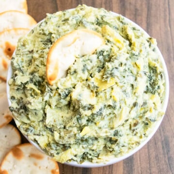 Best easy homemade creamy spinach artichoke dip in white bowl with round crackers.