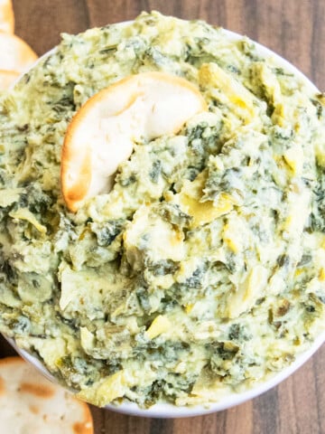Best easy homemade creamy spinach artichoke dip in white bowl with round crackers.