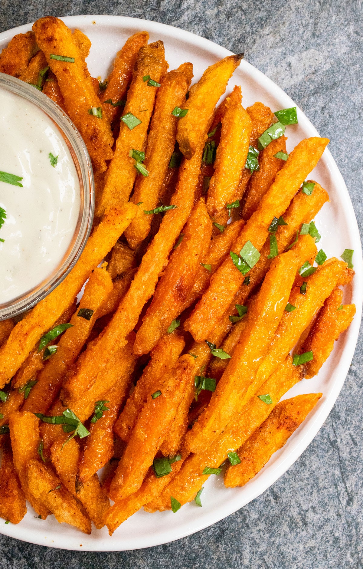 Overhead shot of baked sweet potato sticks in white dish with bowl of ranch sauce. 