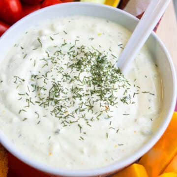 Easy homemade creamy fresh dill dip in white bowl with white spoon on charcuterie tray.