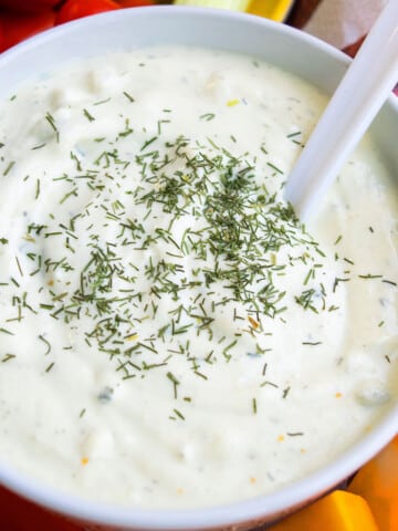 Easy homemade creamy fresh dill dip in white bowl with white spoon on charcuterie tray.