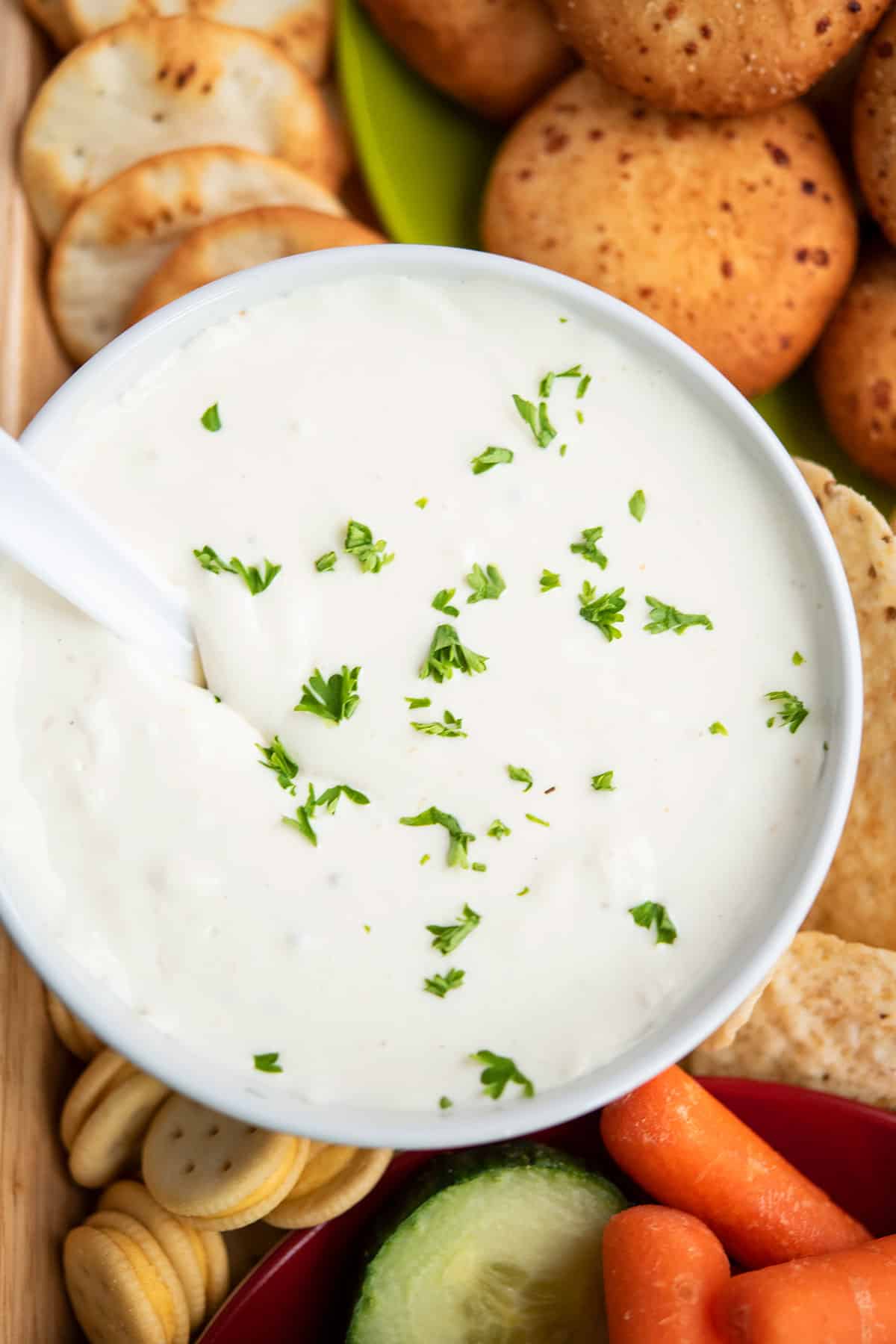 Overhead shot of vegetable dip in white bowl on tray of veggies and crackers. 