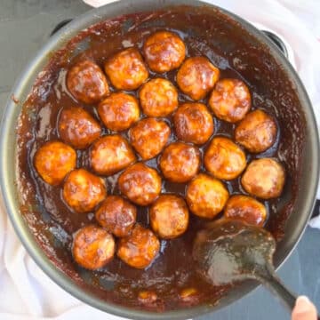 Meatballs being coated in sauce with black spoon.