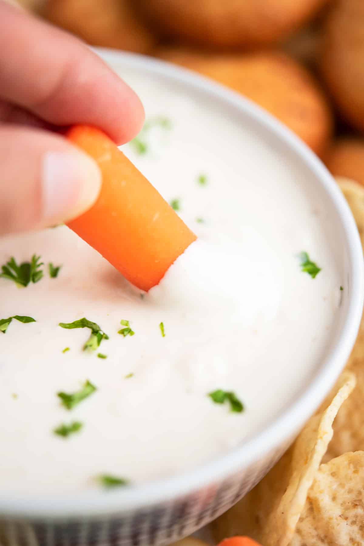 Baby carrot being dunked in creamy appetizer. 