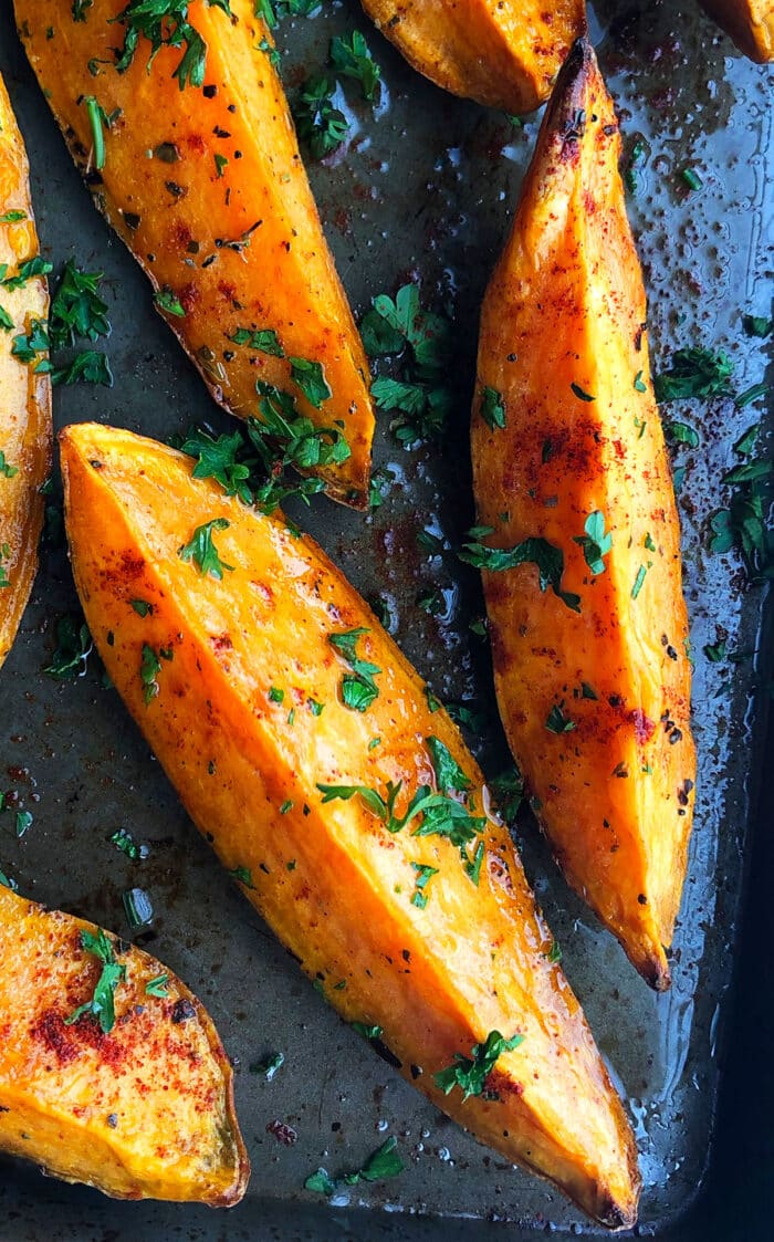Thick roasted sweet potato slices on baking tray with parsley garnish.