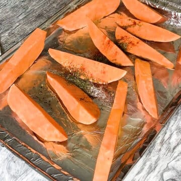 Wedges with seasonings and oil in lined baking tray.