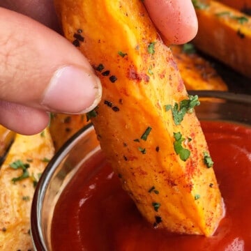 Best easy crispy oven baked or roasted sweet potato wedges being dipped in bowl of ketchup.