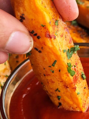 Best easy crispy oven baked or roasted sweet potato wedges being dipped in bowl of ketchup.
