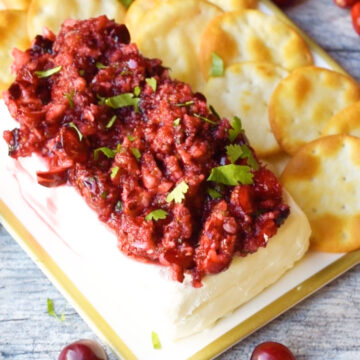 Salsa spooned over block of cream cheese and presented on a tray with crackers. 