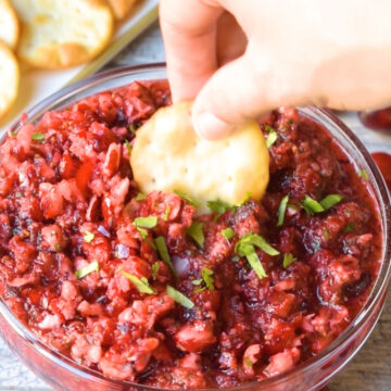 Cracker being dipped in bowl of red salsa. 