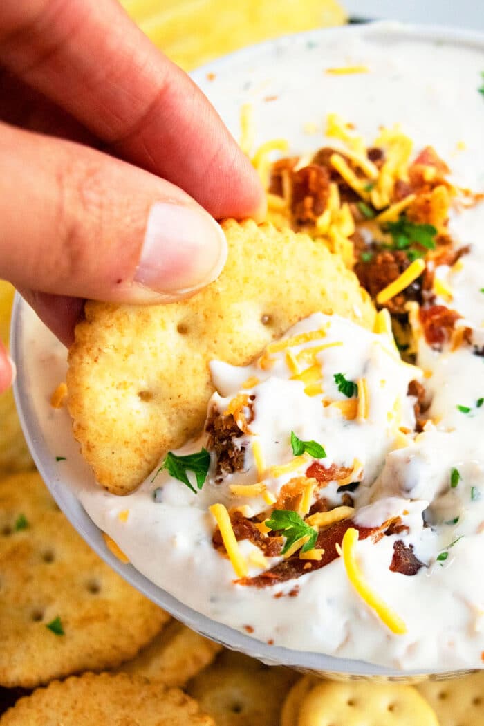 Cracker being dipped into bowl of easy Bacon Cheddar Ranch Dip.