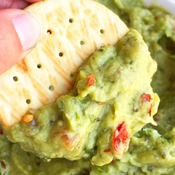 Cracker dipped in bowl of best easy homemade guacamole dip- Closeup shot.