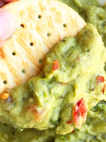 Cracker dipped in bowl of best easy homemade guacamole dip- Closeup shot.