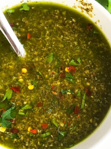 Bowl of easy homemade Argentinian green chimichurri sauce with parsley, cilantro and oregano-Overhead shot.