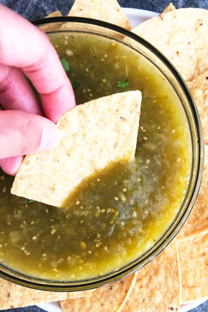 Tortilla chip being dipped in bowl of green tomatillo salsa.