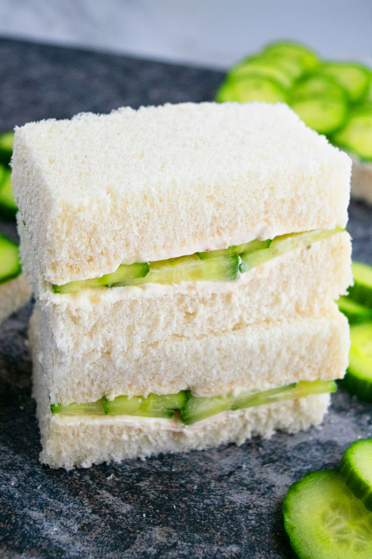 Stack of best easy cucumber sandwiches with garlic herb cream cheese on gray background. 