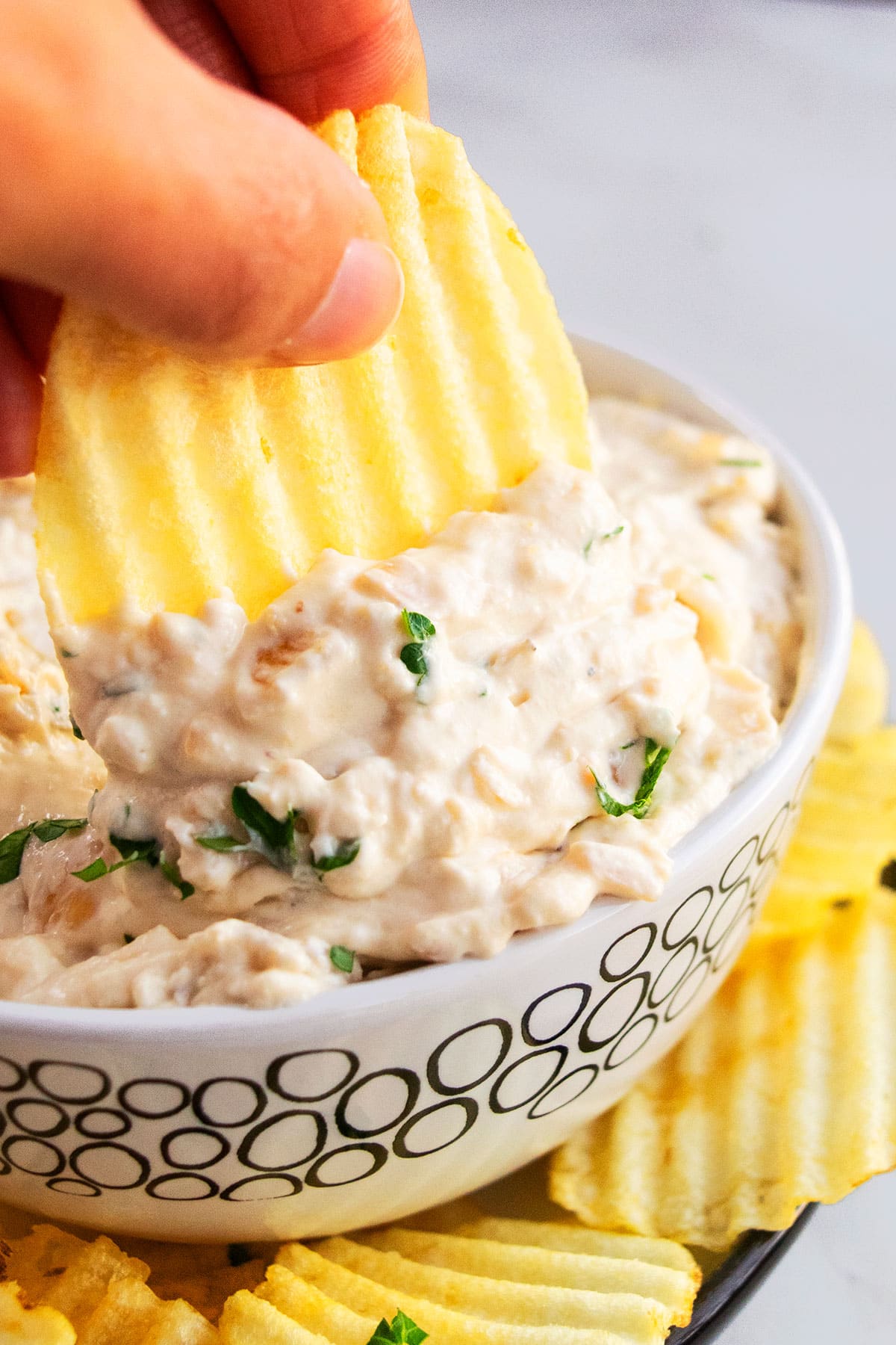 Potato chip being dipped into bowl of easy french onion dip in white bowl.  