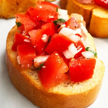Best easy Italian bruschetta with tomatoes on toasted bread with mozzarella cheese topping on white marble background.