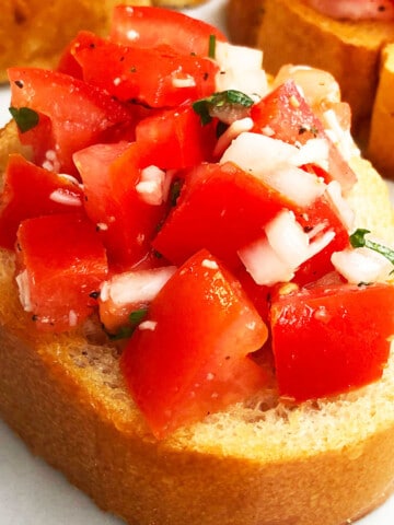 Best easy Italian bruschetta with tomatoes on toasted bread with mozzarella cheese topping on white marble background.