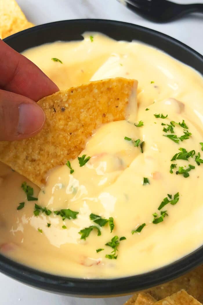 Bowl of creamy dip with tortilla being dunked in. 