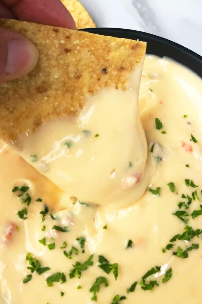 Tortilla being dipped in easy homemade Mexican queso dip. 