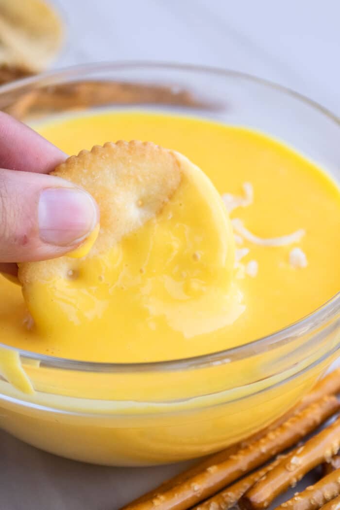 Cracker Being Dipped in a Bowl of Creamy Velveeta Sauce. 